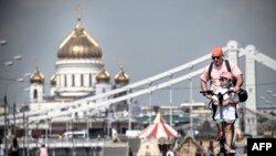 Muškarac i dijete voze se električnim skuterom duž nasipa rijeke Moskve, a u pozadini je katedrala Hrista Spasitelja u Moskvi 6. avgusta 2023.