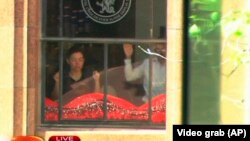 FILE - This image taken from video shows people holding up hands inside the Lindt Chocolate Cafe in Sydney, Dec. 15, 2014. 