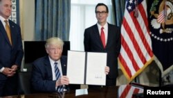 U.S. President Donald Trump displays a financial services executive order as Treasury Secretary Steven Mnuchin looks on during a signing ceremony at the Treasury Department in Washington, April 21, 2017.