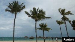 FILE - People walk along a beach in Nassau, Bahamas.