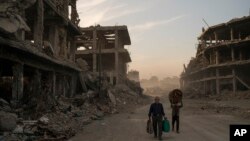 FILE - Haider (L) and Abdullah carry belongings they collected from their damaged house to wash before returning to live in the Old City of Mosul, Iraq, Nov. 15, 2017. 