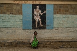 A woman sits in front during a science lesson painted on a wall of one school now housing displaced families, in Mekelle, Ethiopia, June 3, 2021. (Yan Boechat/VOA)