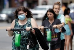 A woman wears a mask as she rides a scooter, June 30, 2020, in Nashville, Tenn.