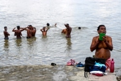 FILE - A man trims his beard while others bathe in the Hooghly River in Kolkata, India, Sept. 3, 2020. India has been reporting the highest single-day coronavirus caseload in the world every day for more than three weeks.