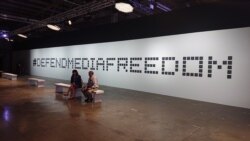 Two journalists relax in front of plaques memorializing journalists killed since 2016. The display was part of the Global Conference for Media Freedom.