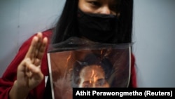 A demonstrator flashes a three-finger salute while holding a picture of Aung San Suu Kyi as Myanmar citizens living in Thailand protest against the military coup, outside Myanmar embassy in Bangkok, Thailand February 4, 2021.