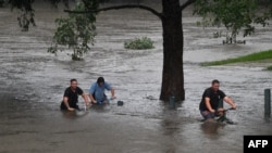 Orang-orang mengendarai sepeda melalui sebuah taman yang tergenang banjir di tepi sungai Nepean di pinggiran Penrith, saat kota Sydney, Australia, bersiap menghadapi banjir terburuk dalam beberapa dekade, Minggu 21/3. (Foto: AFP)