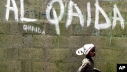 FILE - A girl walks past a wall with graffiti about the al-Qaida network in Kano, Nigeria, April 18, 2003. An airstrike this week by U.S. forces and the Libyan government targeted Al-Qaida in the Islamic Maghreb, southeast of Bani Walid, Libya.
