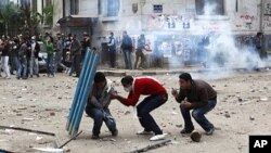 Protesters hide behind a portion of a fence as police fire tear gas and throw stones back at protesters, who have been throwing stones at the police, near Tahrir Square in Cairo Egypt, November 20, 2011.