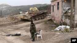 Syrian troops stand, with a destroyed tank in the background, on a street in Salma, Syria, Jan. 22, 2016. Syrian government forces, relying on Russian air cover, have recently seized Salma, located in Syria's province of Latakia, from militants.