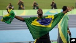 Usain Bolt de la Jamaïque bras étendus, couvert du drapeau brésilien et tenant le drapeau de son pays en main, célèbre après avoir remporté la médaille d'or en finale du 4x100 mètres relais messieurs lors des compétitions d'athlétisme des Jeux Olympiques d'été de 2016 au stade olympique de Rio de Janeiro, au Brésil, 19 août 2016. 