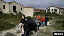 FILE - Afghan refugees walk through a beach where they will wait to board a dinghy sailing off for the Greek island of Chios, while they try to travel from the western Turkish coastal town of Cesme, in Izmir province, Turkey, March 6, 2016. 