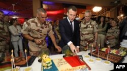 Le président français Emmanuel Macron coupe un gâteau couvert des couleurs du drapeau français lors d’un dîner de Noël avec quelque 700 soldats français de la force anti-djihadiste française sur la base aérienne française de la force Barkhane à Niamey, Ni