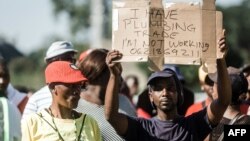FILE - An unemployed man holds up a sign at the Sugar Ray Xulu stadium in Clermont township, north of Durban, May 1, 2019. (Photo by RAJESH JANTILAL / AFP)
