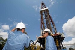 FILE - Workers stand near an oil drilling rig belonging to Petroamazonas at Miranda Port in Tiputini, Ecuador, Sept. 7, 2016.