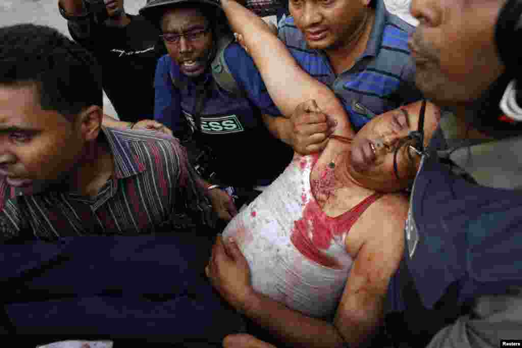 Members of the media assist an injured police officer during a clash with activists of Hifazat-e-Islam in front of the national mosque in Dhaka, May 5, 2013.