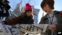 Japanese women react as they read extra newspapers in Tokyo reporting about an online video that purported to show an Islamic State group militant beheading Japanese journalist Kenji Goto, Sunday morning, Feb. 1, 2015. 