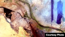 Smoke drifts south in this image of Al Basrah, located in southeastern Iraq, captured by the Landsat mission on April 4, 2003. The green circles from the center to the left of the image represent irrigated crops. (Courtesy USGS)