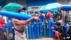 A man carries an oxygen tank as he walks past people waiting with oxygen tanks in need of refill outside the Naing oxygen factory at the South Dagon industrial zone in Yangon, Myanmar, July 28, 2021. 