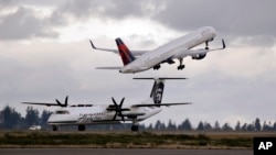 FILE - A Delta jet takes off in view of an Alaska Airlines plane that just landed at Seattle-Tacoma International Airport in Washington, Dec. 16, 2015. 