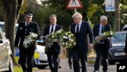 British Prime Minister Boris Johnson and leader of the Labour Party Keir Starmer, second from left, carry flowers as they arrive at the scene where member of parliament David Amess was stabbed Friday, in Leigh-on-Sea, Essex, England, Oct. 16, 2021. 