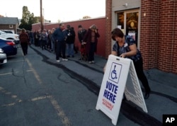 FILE - An election official places a sign as voters line up outside a polling place at the Fogelsville Volunteer Fire Co., Tuesday, Nov. 8, 2016, in Fogelsville, Pa. (AP Photo/Matt Slocum)