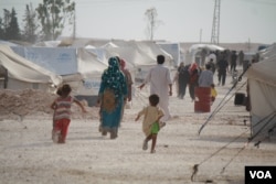 FILE - Families walk by tents in a camps for displaced persons in Ain Issa, Syria, Aug. 17, 2017. (H. Murdock/VOA)