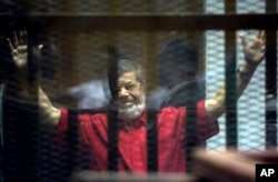 Former Egyptian President Mohamed Morsi, wearing a red jumpsuit that designates he has been sentenced to death, raises his hands inside a defendants cage in a makeshift courtroom at the national police academy, in an eastern suburb of Cairo, Egypt, Saturd