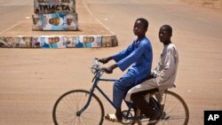 Two boys riding a bicycle pass by campaign posters for opposition candidate Gen. Muhammadu Buhari on a roundabout in Daura, his home town, in Katsina state in northern Nigeria, March 27, 2015. 