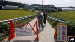 Quarantine officials wear protective gear as a precaution against African swine fever at a pig farm in Paju, South Korea, Sept. 17, 2019. The notice reads: "Under quarantine."