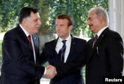 FILE - French President Emmanuel Macron stands between Libyan Prime Minister Fayez al-Sarraj, lefr, and General Khalifa Haftar, commander in the Libyan National Army), who shake hands after talks over a political deal to help end Libya's crisis in La Celle-Saint-Cloud near Paris, France, July 25, 2017.