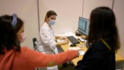 Maria do Carmo, 8, left, quickly points at her sister Madalena, 11, when nurse Catarina, center, asks which of them will be first to take their shots of the vaccine against COVID-19 at a vaccination center in Lisbon, Saturday, Dec. 18, 2021.