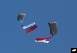 FILE - Serbian soldiers parachute from a Mi-8 transport helicopter with a Russian, left, and Serbian flags during joint Russian-Serbian military exercices at Nikinci training ground, 60 kilometers west of Belgrade, Serbia, Nov. 14, 2014.