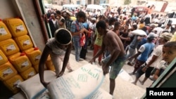 Workers unload sacks of wheat flour as people gather outside an aid distribution center in the Red Sea port city of Hodeida, Yemen, June 14, 2018. 