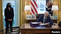 U.S. President Joe Biden signs the American Rescue Plan, a measure to respond to the impact of the coronavirus pandemic, inside the Oval Office at the White House in Washington, U.S., March 11, 2021. Standing at left is Vice President Kamala Harris. (REUTERS/Tom Brenner)
