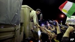 FILE - A Kurdish Peshmerga solider reaches out his hand to supporters at a border crossing in Iraq, Oct. 29, 2014. 