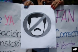 People hold a sign with a no symbol over an image representing President Nicolas Maduro as they take part in a walk out against Maduro, in Caracas, Venezuela, Jan. 30, 2019.