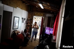Miguel Rosario Lopez watches a television that works using electricity from a generator on Dec. 11, 2017, while his wife Milagros Jimenez walks through their house, which was partially destroyed by Hurricane Maria.