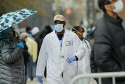 A medical worker walks past people lined up at Gotham Health East New York, a COVID-19 testing center, April 23, 2020, in the Brooklyn borough of New York.