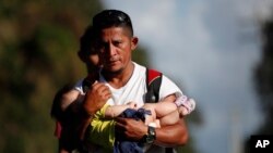 Imigran asal Honduras, Selvin Hernández, menggendong anak seorang migran lainnya, saat rombongan mereka berusaha mencapai Amerika Serikat, di El Cinchado, Guatemala, dekat Honduras, Rabu, 15 Januari 2020. (Foto: AP)