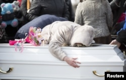 在为一名克麦罗沃商城火灾受害者举行的葬礼期间，一位女士在墓地抚棺痛苦。（2018年3月28日）