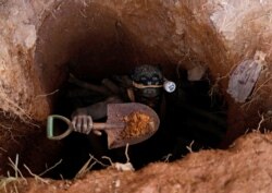 FILE - A miner carries a shovel as he climbs out from inside a gold-mining pit at the site of Nsuaem-Top, Ghana, Nov. 24, 2018.