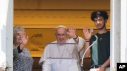 Paus Fransiskus (tengah) didampingi oleh dua orang jemaat menyapa para jemaat lainnya dari jendela kediamannya di Lapangan St. Peter di Vatikan, pada 23 Juli 2023. (Foto: AP/Andrew Medichini)