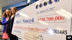 Mavis Wanczyk, of Chicopee, Mass., stands by a poster of her winnings during a news conference where she claimed the $758.7 million Powerball prize at Massachusetts State Lottery headquarters, Aug. 24, 2017, in Braintree, Mass. At left is state Treasurer 