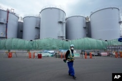 FILE - A worker helps direct a truck driver as he stands near tanks used to store treated radioactive water after it was used to cool down melted fuel at the Fukushima Daiichi nuclear power plant, run by Tokyo Electric Power Company Holdings (TEPCO), in Okuma town, northeastern Japan, Thursday, March 3, 2022.
