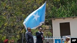 Somalia's President Mohamed Abdullahi Farmajo, center-right, holds a Somali flag during a handover ceremony at the presidential palace with former president Hassan Sheikh Mohamud, center-left, in Mogadishu, Somalia Thursday, Feb. 16, 2017. 