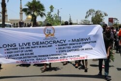 Protestors carry a banner along Kamuzu High Way In Blantyre. (Lameck Masina/VOA)