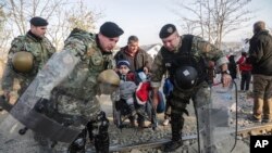 Petugas kepolisian di perbatasan Makedonia membantu seorang migran anak-anak yang menggunakan kursi roda di Gevgelija (Foto: dok). 