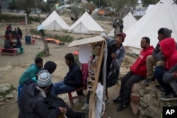 Pakistani men charge their mobile phones in a makeshift migrant camp made by volunteers near the village of Moria, Lesbos island , Greece, March 22, 2016.