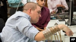 In this September 2014 photo provided by Ohio State University, Ian Burkhart participates in a study with neural bypass technology at The Ohio State University Wexner Medical Center in Columbus. A computer chip in Burkhart's brain reads his thoughts, decodes them, then sends signals to a sleeve on his arm, that allows him to move his hand. (Jo McCulty/Ohio State University Wexner Medical Center via AP)